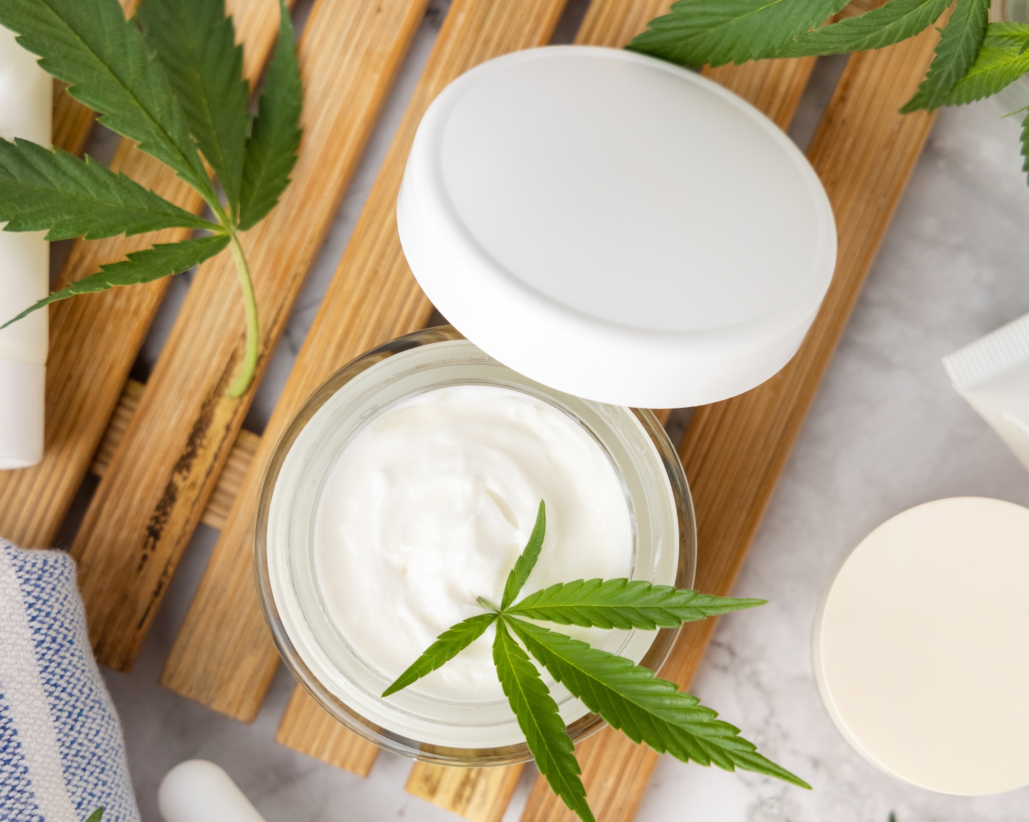 Opened cream jar with green cannabis leaves top view, organic natural CBD cosmetic